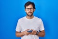 Handsome latin man using smartphone typing message winking looking at the camera with sexy expression, cheerful and happy face Royalty Free Stock Photo