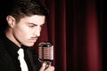 Handsome latino singer performs in front of vintage microphone in nightclub with red curtain in background