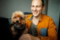 Handsome laughing man using laptop with dog at home.