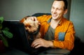 Handsome laughing man using laptop with dog at home.