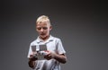 Handsome little boy boxer with blonde hair dressed in a white t-shirt holds a quadcopter control remote.