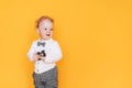 Handsome little boy in front of yellow background in white shirt and bow tie. Kid holding gift flowers for mother in hands Royalty Free Stock Photo