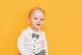 Handsome little boy in front of yellow background in white shirt and bow tie. Kid holding gift flowers for mother in hands Royalty Free Stock Photo