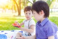 Handsome little boy looking at camera during he playing toy at park and staying with older brother. Lovely kid is adorable or look