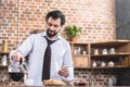 handsome loner businessman pouring coffee into cup and holding smartphone