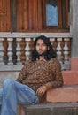 A handsome long haired Indian young men looking at camera, posing with sitting on temple stairs Royalty Free Stock Photo