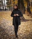 Handsome long haired man in black trench coat walking in the park in wonderful autumn day Royalty Free Stock Photo