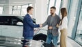 Handsome male car buyer is getting key fob from friendly salesman and shaking hands with him while standing beside auto Royalty Free Stock Photo