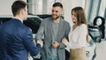 Handsome male car buyer is getting key fob from friendly salesman and shaking hands with him while standing beside auto Royalty Free Stock Photo