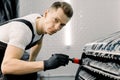 Handsome male car wash worker looking at camera, while cleaning a car grille with a special brush in a vehicle detailing