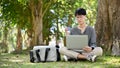 Handsome male college student wearing glasses, sipping coffee while using laptop in the park Royalty Free Stock Photo