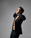 Male with cool hairstyle, in black suit on naked body. He opened his jacket and posing sideways on gray background. Close up Royalty Free Stock Photo