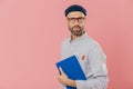 Handsome male designer wears stylish clothes, has two pencils in pocket of shirt, holds blue notepad for making sketches, isolated Royalty Free Stock Photo