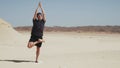 Handsome male doing yoga ardha padma vrikshasana on a rock in desert