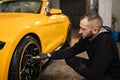 Handsome male employee worker cleaning the wheel tires of modern car by scrubbing brush. Royalty Free Stock Photo