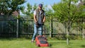 Handsome male gardener mowing grass with an electric lawn mower. Young man mows the grass in own garden with a grass Royalty Free Stock Photo