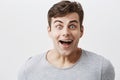 Handsome male in gray t-shirt, smiles with surprisment, looks with bugged blue eyes, being astonished to hear unexpected Royalty Free Stock Photo