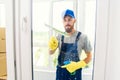 Male janitor using a squeegee to clean a window in an office wearing an apron and gloves as he works