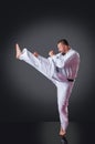 Handsome male karate player doing kick on the gray background