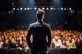 Handsome male motivational speaker holding a microphone in front on an audience. Man in a spotlight talking to a crowd