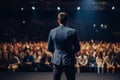 Handsome male motivational speaker holding a microphone in front on an audience. Man in a spotlight talking to a crowd