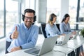 Handsome male online support agent with headset showing thumb up accompanied with his colleagues at call center Royalty Free Stock Photo