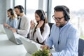 Handsome male operator with headset using laptop computer and working together with other customer support agents in office Royalty Free Stock Photo