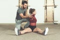 Handsome male personal trainer with a beard helping young fitness girl to stretch her muscles after hard training workout, selecti