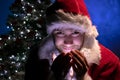 Handsome male santa smiling and holding lights in his hands and looking at camera with christmas tree in background Royalty Free Stock Photo