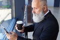 Handsome man age of 50-60 holding cup of coffee and surfing in p Royalty Free Stock Photo