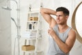 Handsome man applying deodorant to armpit in bathroom, space for text Royalty Free Stock Photo