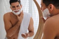 Handsome man applying shaving foam near mirror in bathroom Royalty Free Stock Photo