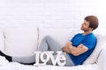 Handsome man arms crossed sitting on white sofa with LOVE alphabet looking at something. Love and Valentine`s Day concept Royalty Free Stock Photo