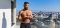 Handsome man with bare chest standing on balcony and enjoying beautiful view on city. Concept of selfcare and enjoying