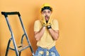 Handsome man with beard by construction stairs wearing hardhat afraid and shocked, surprise and amazed expression with hands on Royalty Free Stock Photo