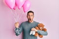 Handsome man with beard expecting a baby girl holding balloons, shoes and teddy bear afraid and shocked with surprise and amazed Royalty Free Stock Photo