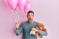 Handsome man with beard expecting a baby girl holding balloons, shoes and teddy bear celebrating crazy and amazed for success with Royalty Free Stock Photo