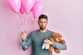 Handsome man with beard expecting a baby girl holding balloons, shoes and teddy bear depressed and worry for distress, crying Royalty Free Stock Photo