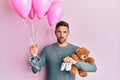 Handsome man with beard expecting a baby girl holding balloons, shoes and teddy bear relaxed with serious expression on face Royalty Free Stock Photo