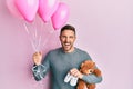 Handsome man with beard expecting a baby girl holding balloons, shoes and teddy bear smiling and laughing hard out loud because Royalty Free Stock Photo