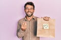 Handsome man with beard holding delivery paper bag with heart reminder doing money gesture with hands, asking for salary payment, Royalty Free Stock Photo