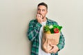 Handsome man with beard holding paper bag with groceries looking stressed and nervous with hands on mouth biting nails Royalty Free Stock Photo