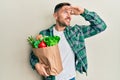 Handsome man with beard holding paper bag with groceries very happy and smiling looking far away with hand over head Royalty Free Stock Photo