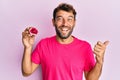 Handsome man with beard holding pink geode precious gemstone pointing thumb up to the side smiling happy with open mouth