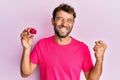 Handsome man with beard holding pink geode precious gemstone screaming proud, celebrating victory and success very excited with