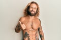 Handsome man with beard and long hair standing shirtless showing tattoos doing happy thumbs up gesture with hand Royalty Free Stock Photo