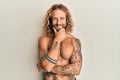 Handsome man with beard and long hair standing shirtless showing tattoos looking confident at the camera smiling with crossed arms Royalty Free Stock Photo