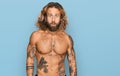 Handsome man with beard and long hair standing shirtless showing tattoos in shock face, looking skeptical and sarcastic, surprised Royalty Free Stock Photo
