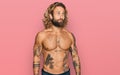 Handsome man with beard and long hair standing shirtless showing tattoos smiling looking to the side and staring away thinking Royalty Free Stock Photo