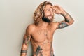 Handsome man with beard and long hair standing shirtless showing tattoos very happy and smiling looking far away with hand over